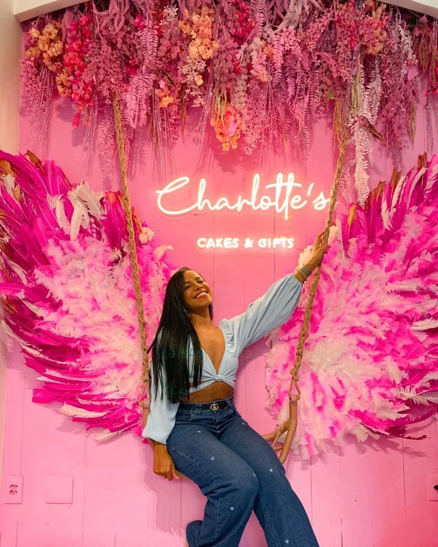 Neon wall setup with feather wings, florals and a swing for a cake and gift shop
